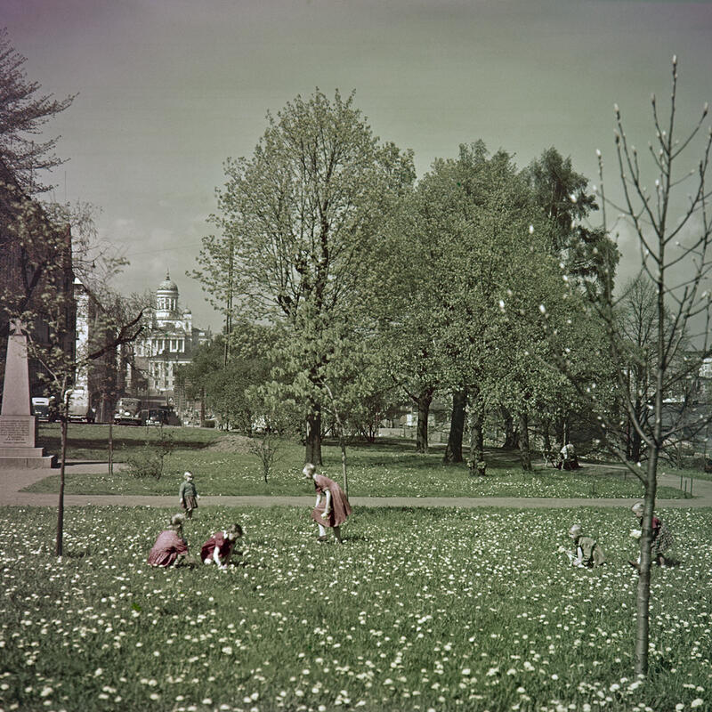 Leikkiviä lapsia Tähtitorninvuoren puistossa. Kuvan reunassa muistopaasi, jonka päällä rautaristi.