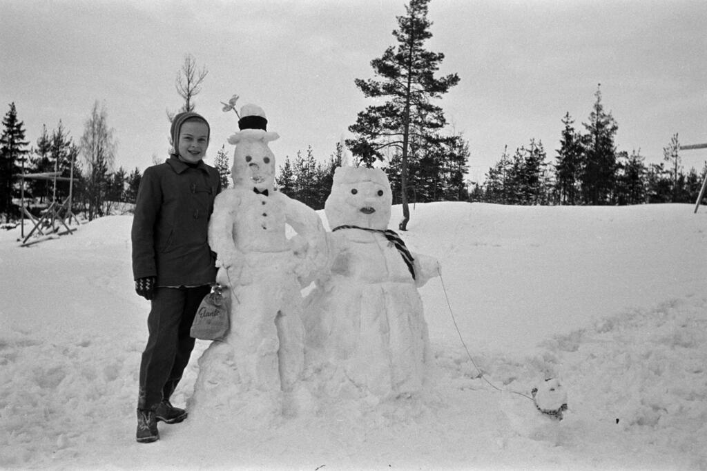 Lapsi on talvella 1958 tehnyt kaksi lumiukkoa ja lumikoiran tai -kissan. Lumiukot esittävät Pekka Puupäätä ja Justiinaa. Kuvaaja: Helsingin kaupunginmuseo / Armas Nyberg