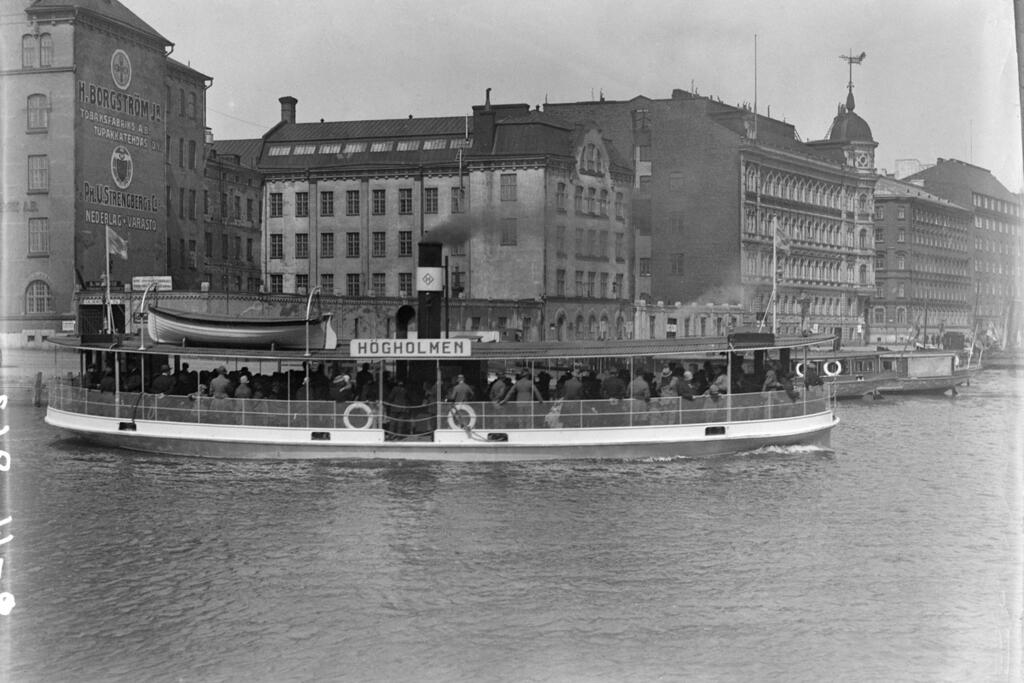 Ända till år 1972 kom man till Högholmen endast vattenledes. Ångbåtar började trafikera år 1883 från Södra hamnen via Norra hamnen till Högholmen. Färjehamnen flyttades från Norra kajen till Salutorget på 1980-talet, när Norra Kajen breddades.  Foto: Museiverket / Alexander Savialoff