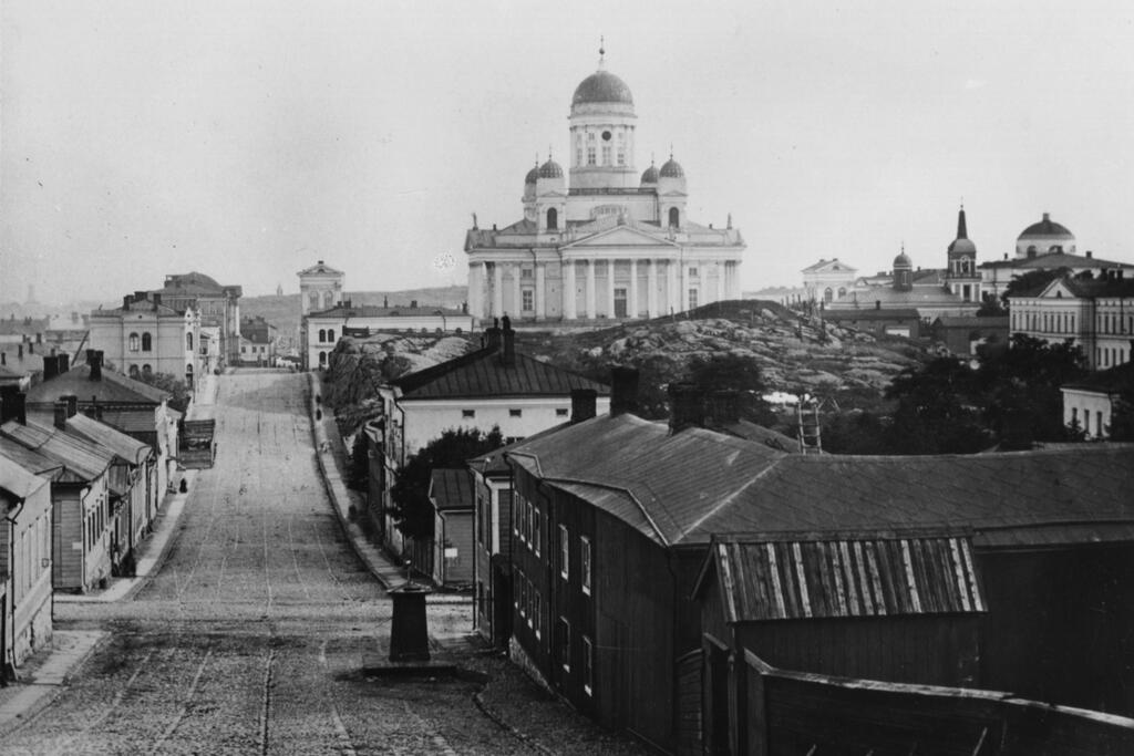 Nikolajgatan (nuv. Snellmansgatan) år 1865. Till höger nummer 8, tidigare Snuskvarnsbacken. Kronohagens sumpiga och bergiga terräng började fyllas ut och schaktas i och med att man på 1830-talet började bygga rätlinjiga gator enligt den nya stadsplanen.  Foto: Helsingfors stadsmuseum