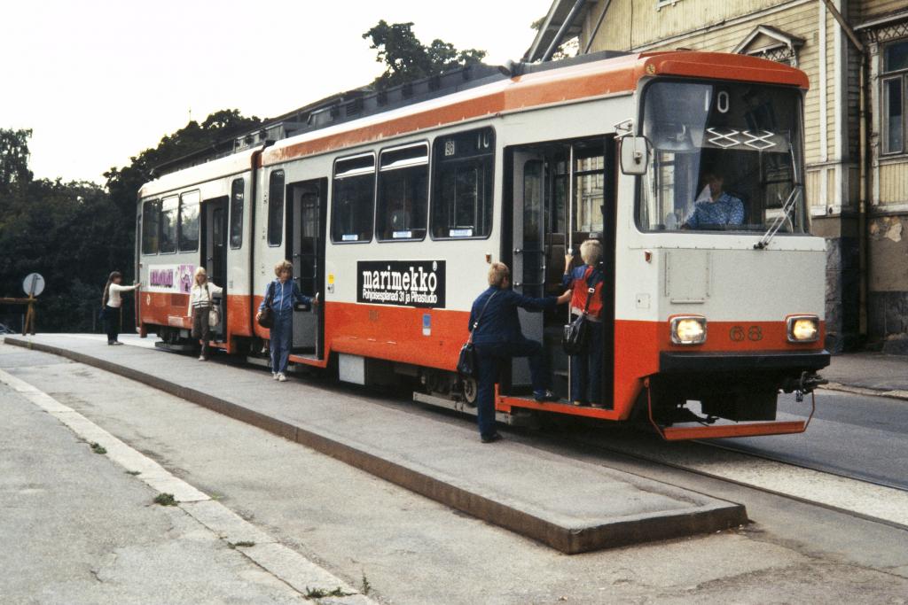 Valmetin valmistamat nivelraitiovaunut otettiin käyttöön vuonna 1973, ja osa niistä on yhä käytössä. Uusi oranssia ja harmaata sisältävä väritys oli tarkoitus ottaa käyttöön kaikissa raitiovaunuissa. Kun kuitenkin metron väriksi myöhemmin valittiin oranssi, päätettiin raitiovaunuille tehdä oma värimaailmansa. Monet kaupunkilaiset ja Helsinki-Seura vaativat takaisin perinteistä keltavihreää väritystä, joka myös saatiin ja on edelleen käytössä.  Kuvaaja: Helsingin kaupunginmuseo / Tuntematon kuvaaja