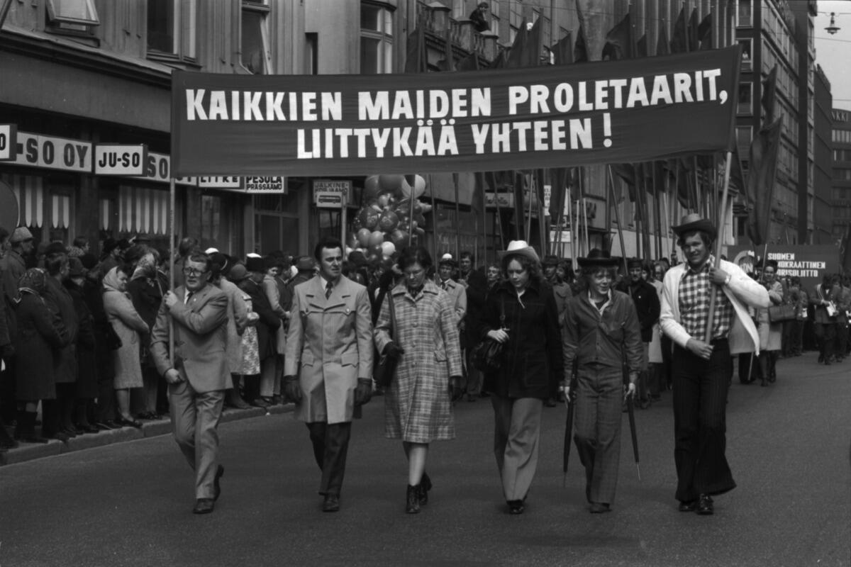 Siltasaarenkatu. Työväen vappumarssi on lähtenyt liikkeelle Hakaniementorilta 1.5.1972. Banderollissa teksti: KAIKKIEN MAIDEN PROLETAARIT, LIITTYKÄÄ YHTEEN! Parilla marssijalla stetson päässä.