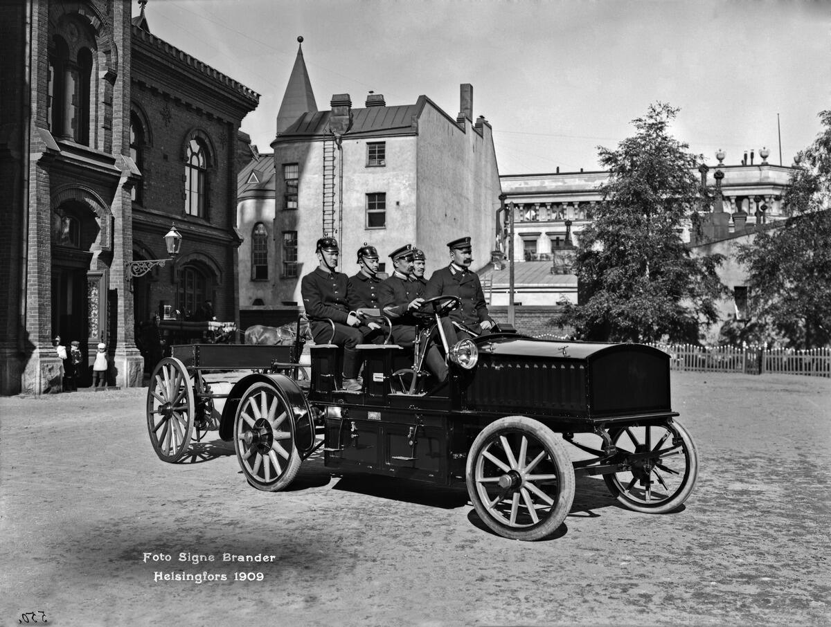 Pääpaloaseman piha, Korkeavuorenkatu 26. Sähköauto vuodelta 1909. Kuljettajana koneenkäyttäjä Flink ja vieressä ruiskumestari Leskinen. 