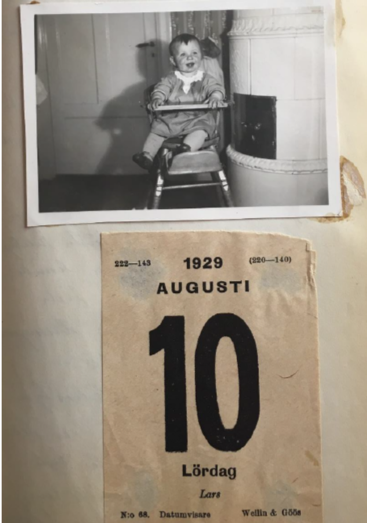 Päiväkirjan sivulla on valokuva nauravasta lapsesta, joka istuu syöttötuolissa kaakeliuunin vieressä. Kuvan alapuolella on almanakasta repäisty lehti, jossa lukea 1929 AUGUSTI 10 Lördag Lars.