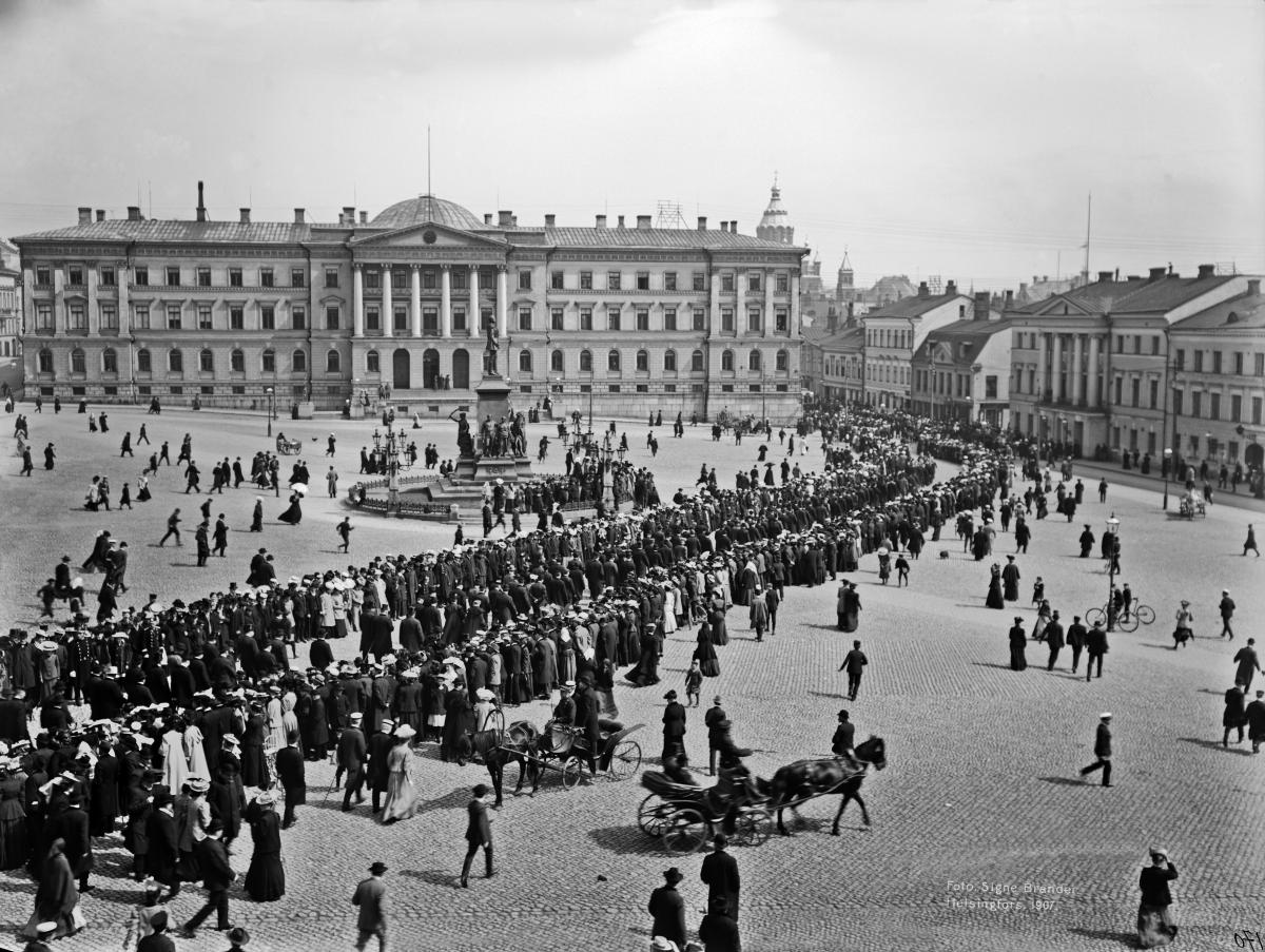 The opening of the first unicameral Diet. Festive procession in the Senate Square on the way from St. Nicholas’ Church to the Imperial Palace (now the Government Palace) on May 25, 1907, with the House of the Senate in the background.  Photo: Helsinki City Museum / Signe Brander