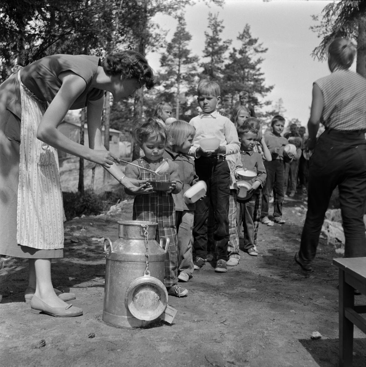 Nainen jakaa jonottaville lapsille keittoa kattilasta leikkipuistossa.