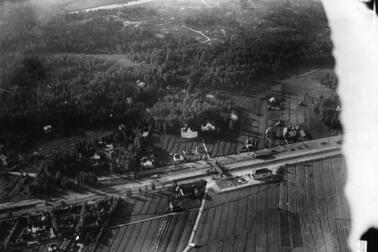 Keskellä kuvaa kulkee junarata, sen ympärillä on rakennuksia mutta enimmäkseen metsää ja peltoja. 