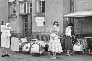 Kesämekkoihin pukeutuneita äitejä, pieniä lapsia ja lastenvaunuja Auroran sairaalan pihalla.