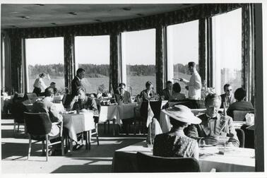 Brändö kasino, Silversundsvägen 49, restaurangsalen och kunder. Serveringspersonal i bakgrunden. Genom fönstren skymtar en havsutsikt.