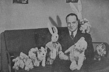 Hymyilevä mies istuu pehmoeläinten ympäröimänä sohvalla.