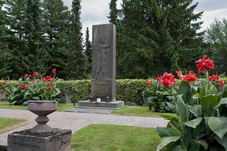Harmaa kivipaasi pystyasennossa, johon kuvattu lippua heiluttava mies.