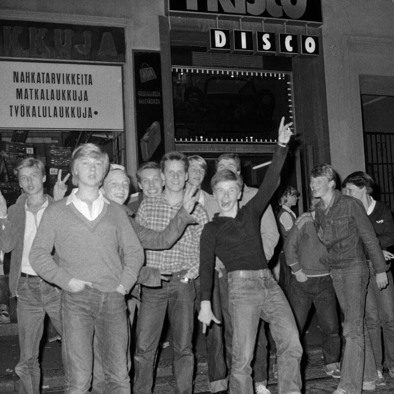 Joukko nuoria poseeraa valokuvaajalle Frisco Disco -tanssiravintolan edustalla vuonna 1978.  Kaikki ovat pukeutuneet farkkuihin, osa niin sanotun fiftarityylin mukaisesti.