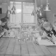 Seitsemän naista työstää hopeaesineitä ison työpöydän ympärillä