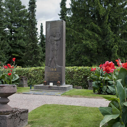 Harmaa kivipaasi pystyasennossa, johon kuvattu lippua heiluttava mies.