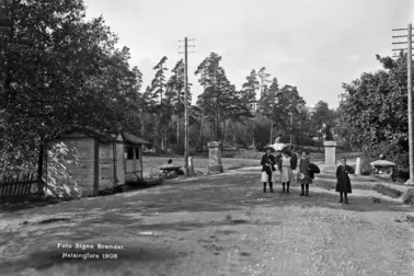 Kaupungin raja, Vanha tulliportti. Läntinen Viertotie 80 (nykyinen Mannerheimintie 108). Neljä lasta seisoo keskellä tietä, taustalla näkyy hevoskärryä ajava mies. Tien vasemmalla puolella on matala puumökki, jonka takana tien kummallakin puolella on kivipaadet, joiden päällä tullinpuomi on aikoinaan levännyt.