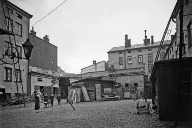 Aleksanterinkatu 52, sisäpiha. Sivuttain katsojaan seisoo nainen, jolla on lapsi sylissä. Kolme isompaa lasta seisoo rivissä keskellä pihaa. 
