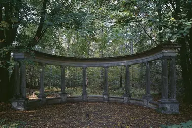 Harmaa pylväskaari metsän keskellä.