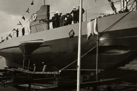 En ubåt fotograferad nerifrån. På däcket står marinsoldater i uniformer.