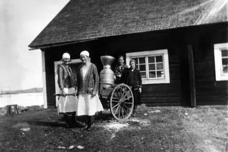 Ladugårdspersonal har samlats framför en låg stockbyggnad med en mjölkkärra.