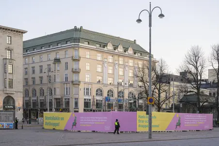 Vy från Norra Esplanaden i riktning mot Södra Esplanaden och Salutorget, där skulpturen Havis Amanda har inhägnats under valborg på grund av de undantagsförhållanden som coronapandemin gav upphov till. Inhägnaden är försedd med följande text: Havis Amanda firar också #vappenhemma! Vi träffas alltså inte här. Helsingfors program för #vappenhemma finns dukad [sic] på nätet. Se Havis Amandas digimösspåläggning, JVG:s gig och allt det andra som erbjuds på helsinkikanava.fi. I bakgrunden syns den byggnad som Arm