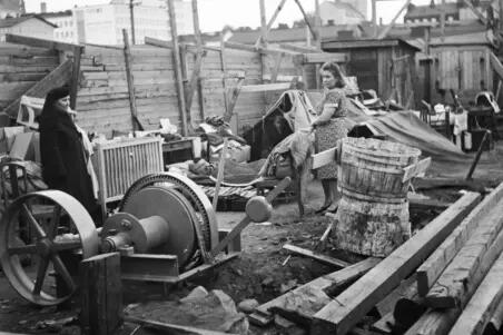 Asunnoton perhe on majoittunut Hakaniemenrantaan vuonna 1950. Kattoa ei ole, paikalla on rakennustarvikkeita, kuten lautakasoja. Taustalla Kalliota ja Kallion kirkko.