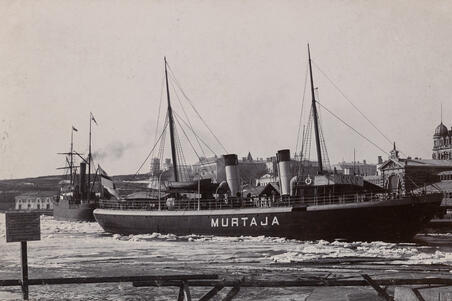 Finlands första isbrytare S/s Murtaja i Södra Hamnen, Norra Kajgrenen (nuvarande Lübeckkajen), framför saluhallen. Fotot togs möjligen i april 1890, då den nybyggda Murtaja anlände till Helsingfors. I vänstra nedre hörnet av bilden finns en skylt där en polis förbjuder att gå på svag is under hot om 4 marks böter.