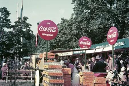 Coca-Colan myyntipiste Hesperian puistossa. Pullokorit täyttävät myyntipisteen edustan, johon on kerääntynyt jonoa.