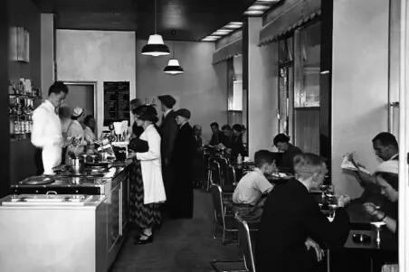 Valion jäätelöbaari Lasipalatsissa, Läntinen Heikinkatu 28 (Mannerheimintie 22-24). Asiakkaita istumassa pöytien ääressä ja seisomassa tiskin luona. Henkilökuntaa tiskin takana.