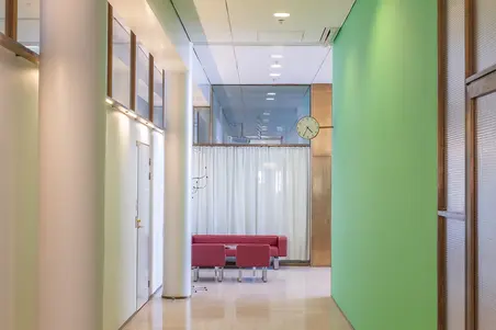 Kuva toimistokäytävästä. Vasemmalla pylväitä ja ovia. Oikealla vihreä seinä sekä kuparikarminen lasiseinä