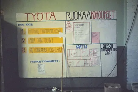 Ilmoitustaulu vallatussa Lepakkoluolassa, jossa neuvotaan talkoisiin osallistumisesta. Taululla otsikot "TYÖTÄ", "RUOKAA" ja "KOKOUKSET". Listattuna päivän työkohteet, edellisen päivän valmiit työt ja rakennuksen kartta.
