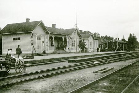 Böles första järnvägsstation fotograferad från sidan av rälsen. Stationen är en träbyggnad med en våning och sadeltak.
