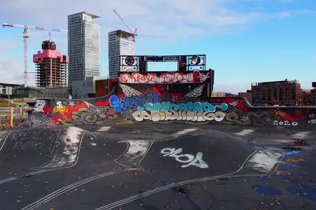 Suvilahti DIY-skeittipuisto. Puistossa betonisia ja asfalttipintaisia kumpareita ja ramppeja, jotka ovat kauttaaltaan värikkäiden graffitien peitossa. Kuvan taustalla kohoaa Kalasataman pilvenpiirtäjien rakennustyömaa.