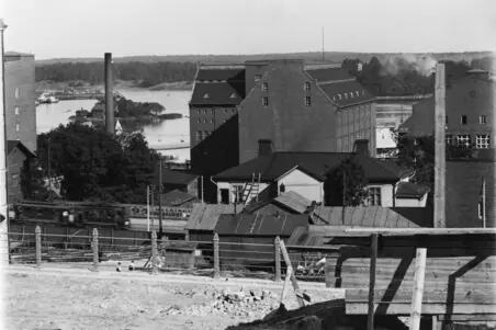 Vy från Terrassgatan 15 mot Tavastvägen 13 och 15, Sörnäs strand och öar (till vänster Hönan, till höger Sumparn). I bakgrunden till höger löper Fågelviksgatan mellan tegelbyggnaderna, längre fram till vänster syns kanten av flervåningshuset på Terrassgatan 17 (Zachrisgatan 3). Till vänster, på andra sidan staketet, ser man en byggarbetsplats på Tavastvägen 38.