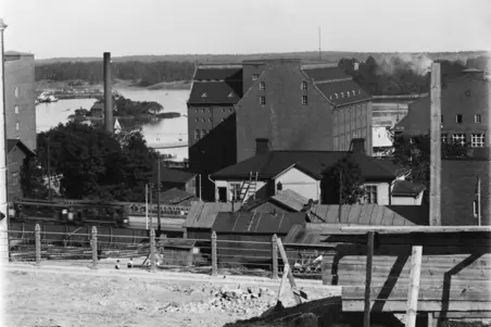 Vy från Terrassgatan 15 mot Tavastvägen 13 och 15, Sörnäs strand och öar (till vänster Hönan, till höger Sumparn). I bakgrunden till höger löper Fågelviksgatan mellan tegelbyggnaderna, längre fram till vänster syns kanten av flervåningshuset på Terrassgatan 17 (Zachrisgatan 3). Till vänster, på andra sidan staketet, ser man en byggarbetsplats på Tavastvägen 38.
