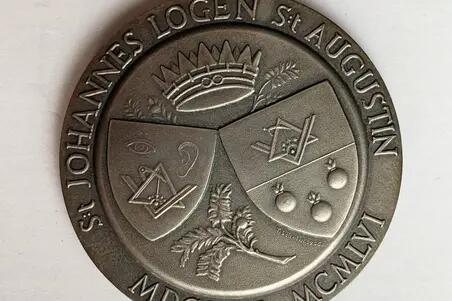 En rund medalj stöpt i silver. På ena sidan löper ett motto längs med övre kanten, på nedre kanten två årstal och frimurarlogens namn.  På medaljens andra sida är en bild av två sköldar med bilder av passare och vinkellinjal. 