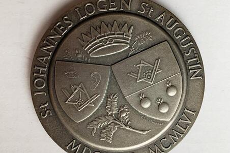 En rund medalj stöpt i silver. På ena sidan löper ett motto längs med övre kanten, på nedre kanten två årstal och frimurarlogens namn.  På medaljens andra sida är en bild av två sköldar med bilder av passare och vinkellinjal. 