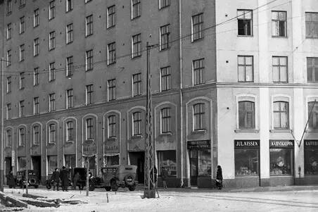 Ett sjuvåningars hus fotograferat från gatan mot hörnet. Det står bilar framför huset. 