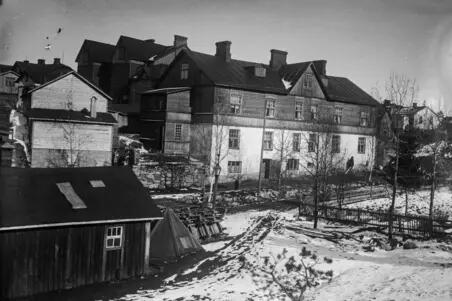 Flervånings bostadshus av trä i Böle i vintrigt landskap i början av 1900-talet. Byggnaden i förgrunden har sadeltak och tre våningar. Husen har byggts tätt intill varandra.