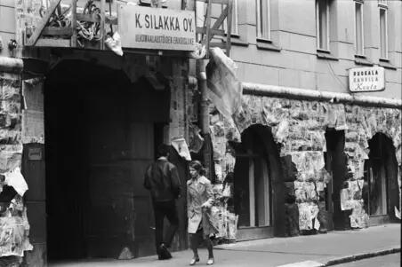 Stenfot som skyddats med tidningar medan målningsarbeten pågår på höghuset på Kronbergsgatan 1. Ovanför portgången finns fasadmålningsföretaget Ulkomaalaustöiden erikoisliike K. Silakka Oy:s målarställning. Till höger Ruokala Kahvila Keulas skylt.