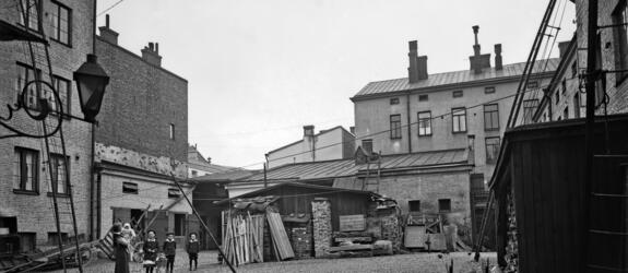 Aleksanterinkatu 52, sisäpiha. Sivuttain katsojaan seisoo nainen, jolla on lapsi sylissä. Kolme isompaa lasta seisoo rivissä keskellä pihaa. 
