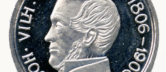 Keskellä hopeanväristä mitalia on miehen profiilikuva. Reunoja kiertää teksti JOH. VILH. SNELLMAN 1806–1906.
