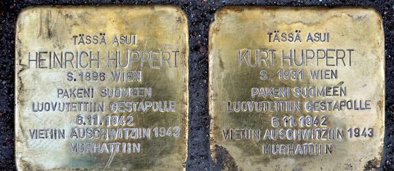 Kaksi metallilaattaa asfaltissa. Niissä tekstit: Tässä asui Heinrich Huppert s 1896 Wien Pakeni Suomeen Luovutettiin Gestapolle 6.11.1942 Vietiin Auschwitziin 1943 Murhattiin