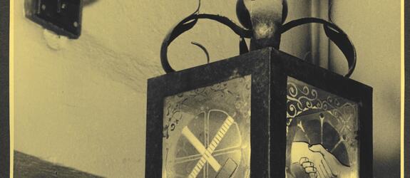 En rektangulär lykta som hänger ovanför en dörr. Lyktan har graverade glasväggar som har dekorerats med frimurarsymboler som en hammare och en måttstock och två händer som håller i varandra.