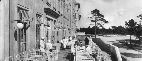 Sairaalarakennuksen terassilla on vieri vieressä sänkyjä, joissa makaa lapsia.