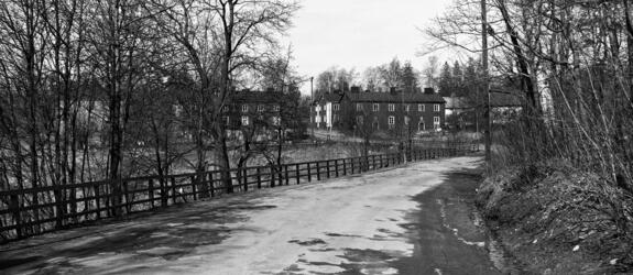 Maantie, jota reunustaa vasemmalla puukaide ja lehdettömät puut. Taustalla näkyy kaksikerroksisia puurakennuksia.