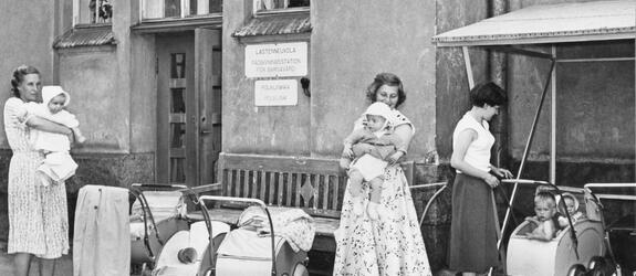 Kesämekkoihin pukeutuneita äitejä, pieniä lapsia ja lastenvaunuja Auroran sairaalan pihalla.