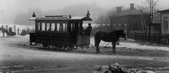 Hästspårvagn på vintern. I bakgrunden hus i dimma.