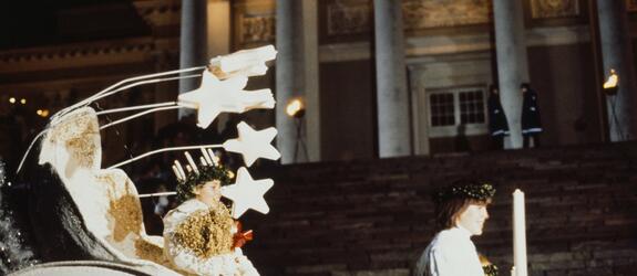 Lucia sitter i en vagn med stjärndekorationer framför Domkyrkan.