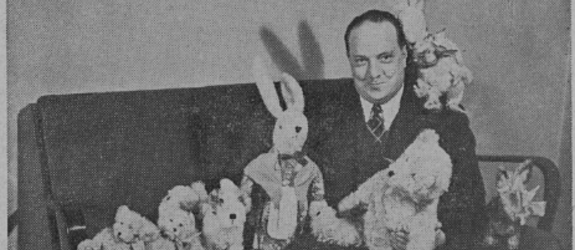 Hymyilevä mies istuu pehmoeläinten ympäröimänä sohvalla.