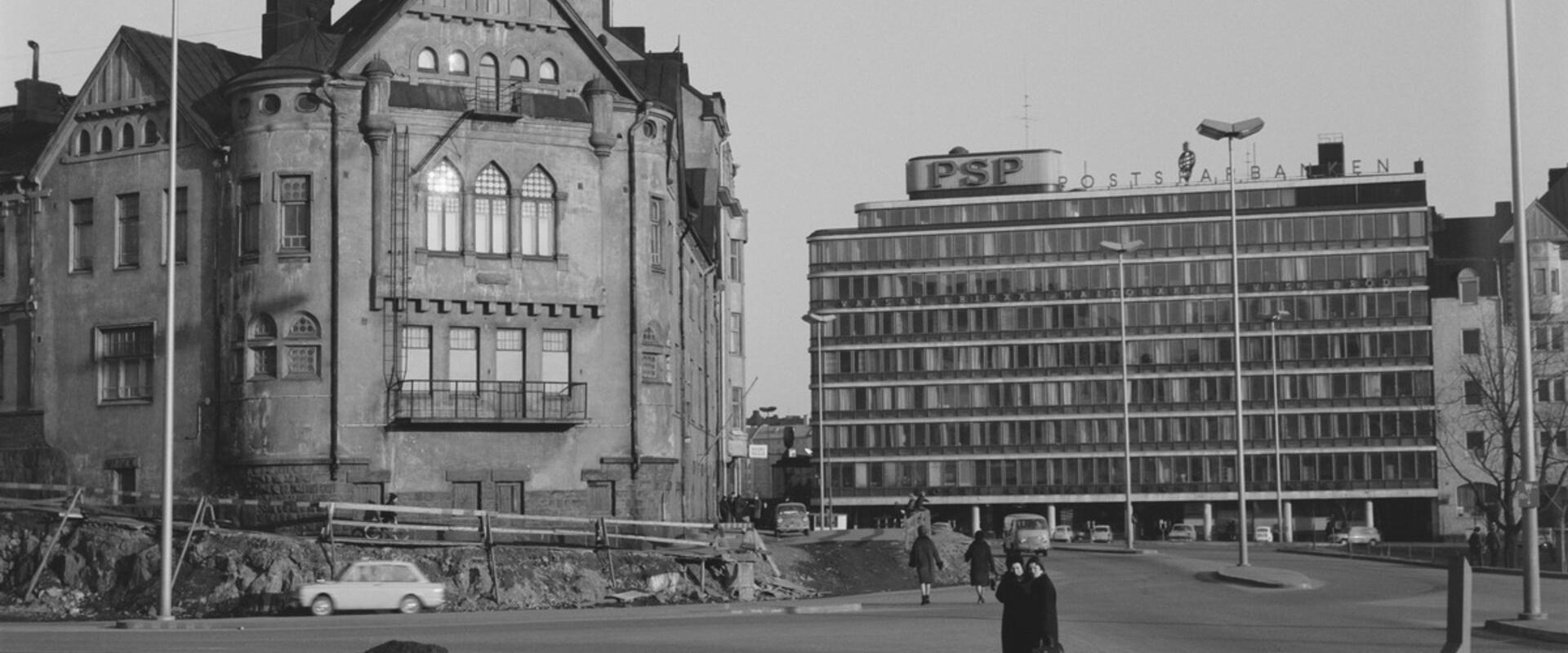 Byggnaden revs kort efter att bilden tagits, och Cirkelhuset stod klart på platsen år 1968. Två förbipasserande har stannat för att titta på bygget av Berghälls ämbetshus, som pågår i förgrunden. Till höger syns Postsparbankens byggnad på Sparbankskajen 2.